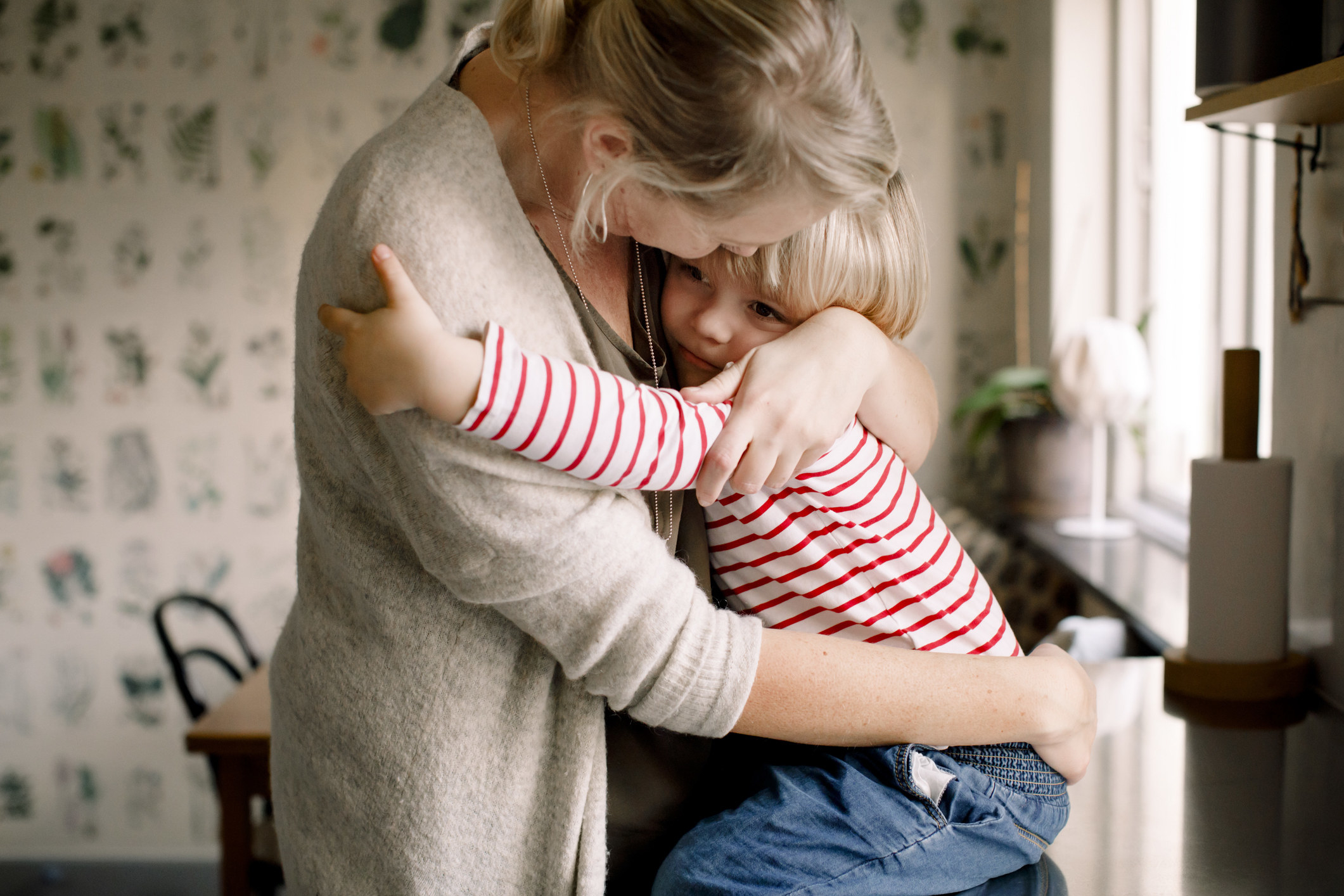 A mother hugs her young child in a kitchen