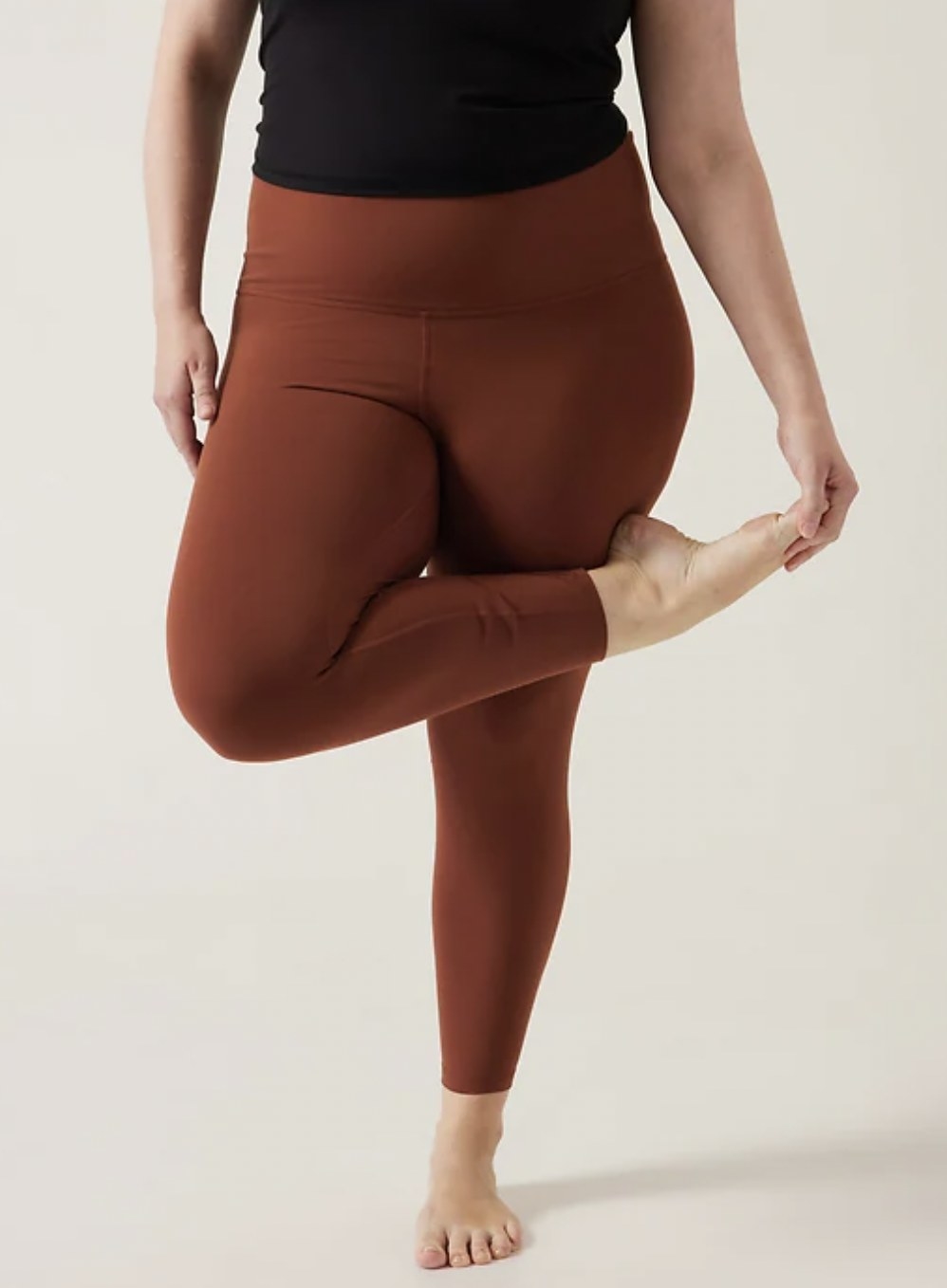Model stretching glute in standing pigeon in copper tights