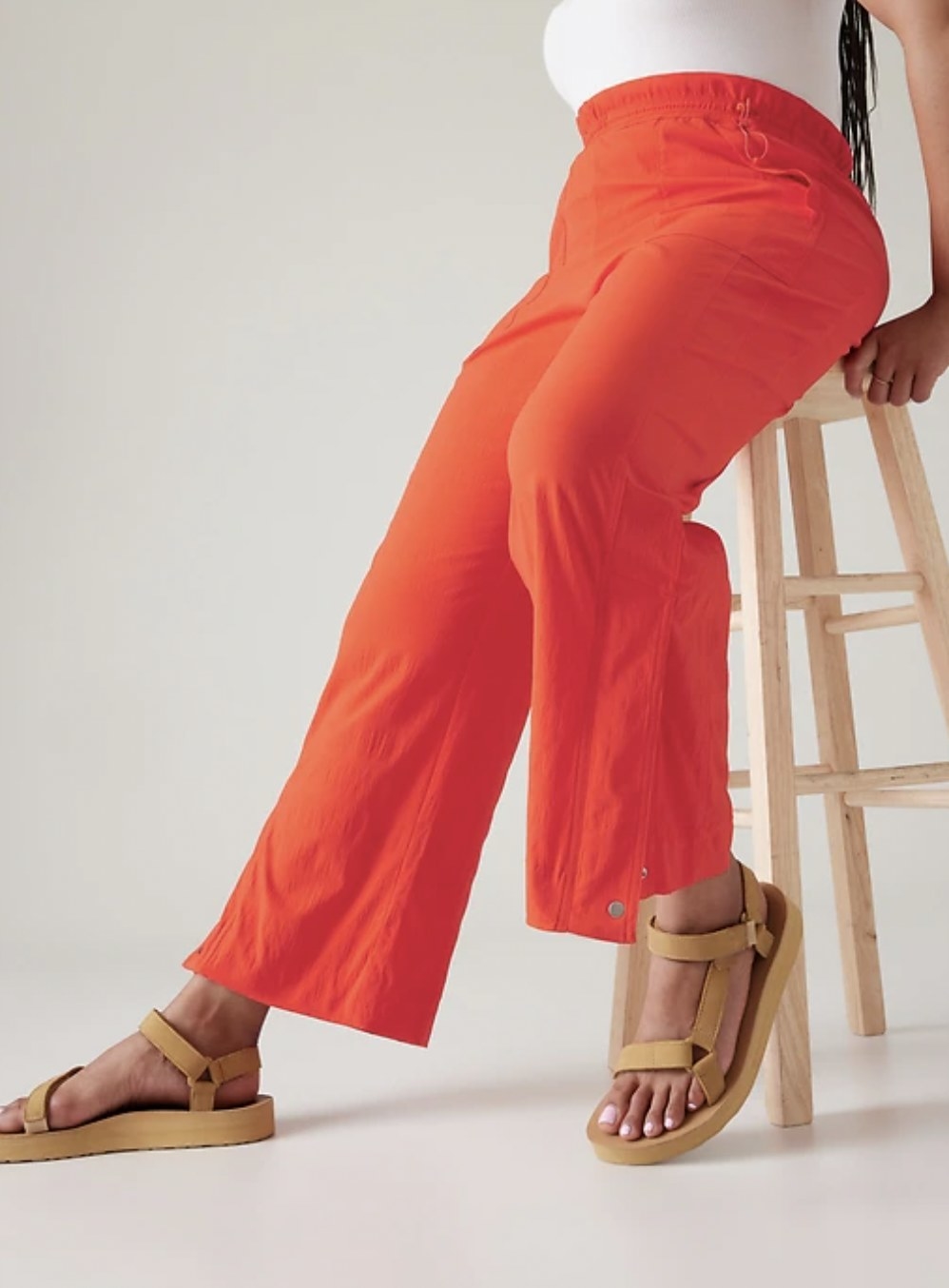 Model sitting on tall stool in orange parachute pants
