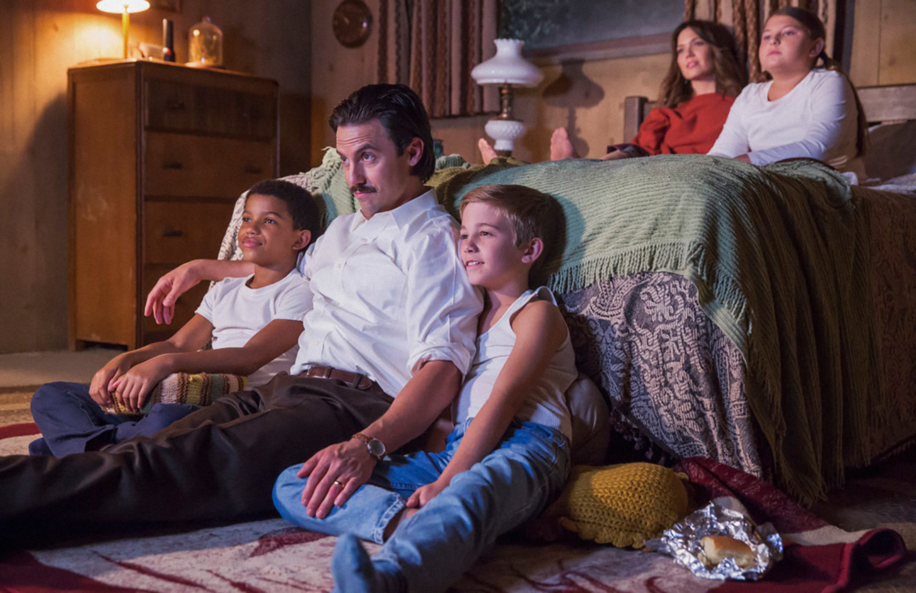 Lonnie Chavis, Milo Ventimiglia, Parker Bates, Mackenzie Hancsicsak, and Mandy Moore watching TV in the bedroom in a scene from This Is Us