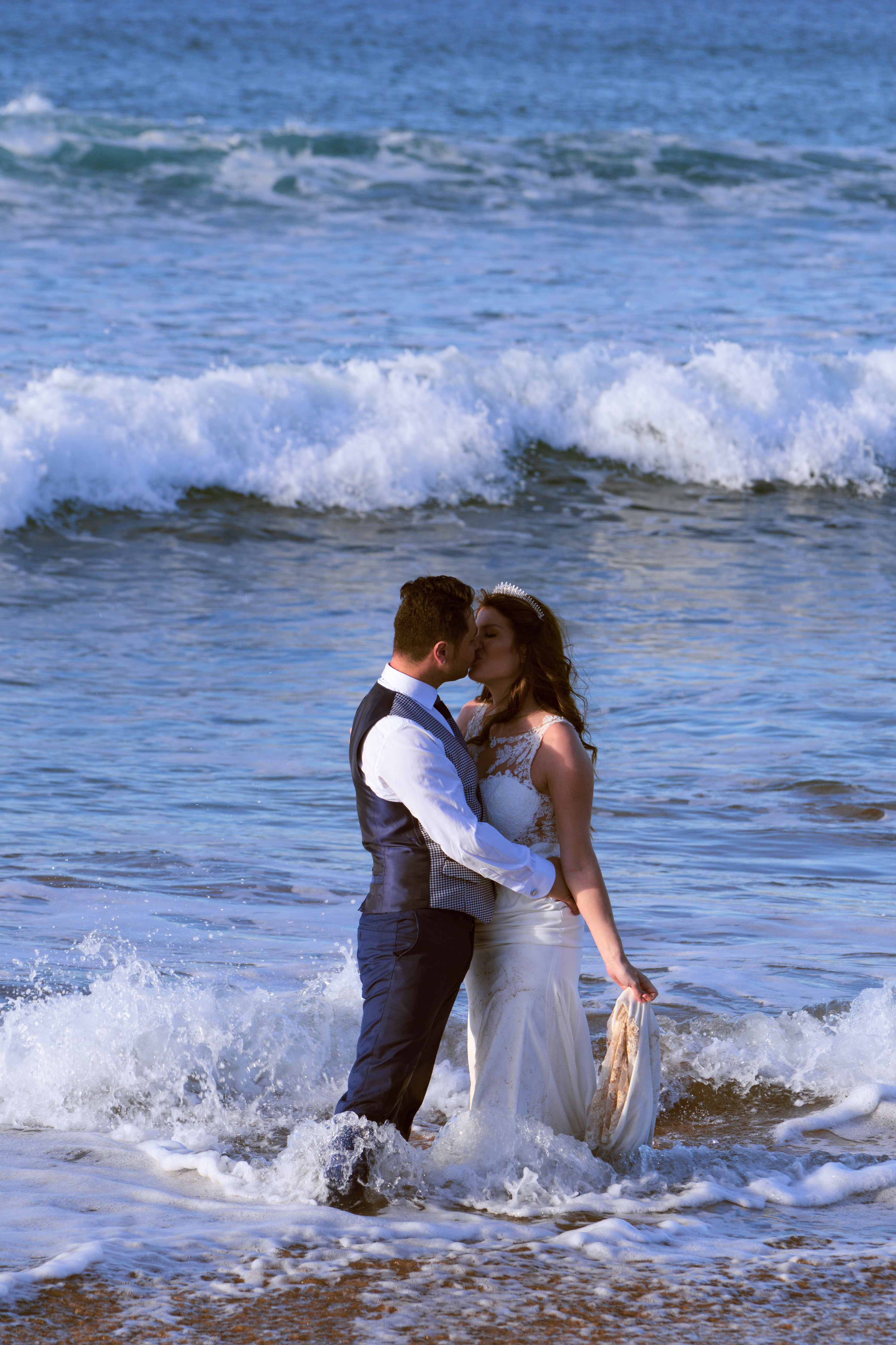 A groom and bride kissing in the water at the beach