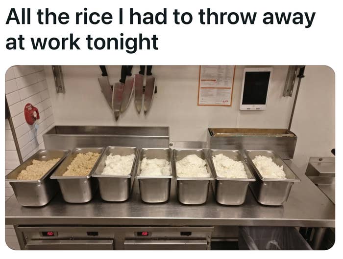 A restaurant's kitchen has seven metal server tubs full of white and brown rice
