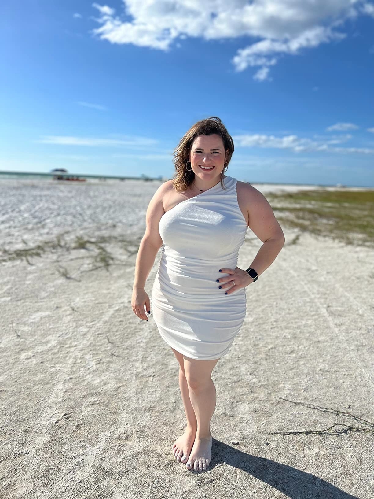 A reviewer wearing the white one shoulder dress at the beach
