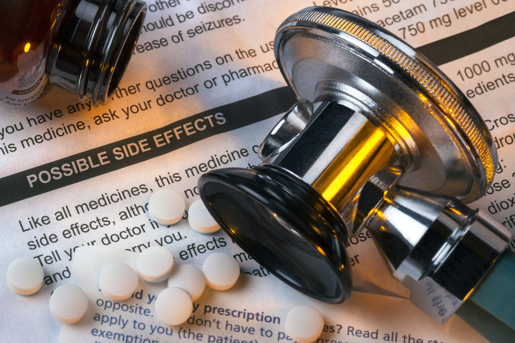 Several pills and a bottle on top of a piece of paper that lists possible side effects