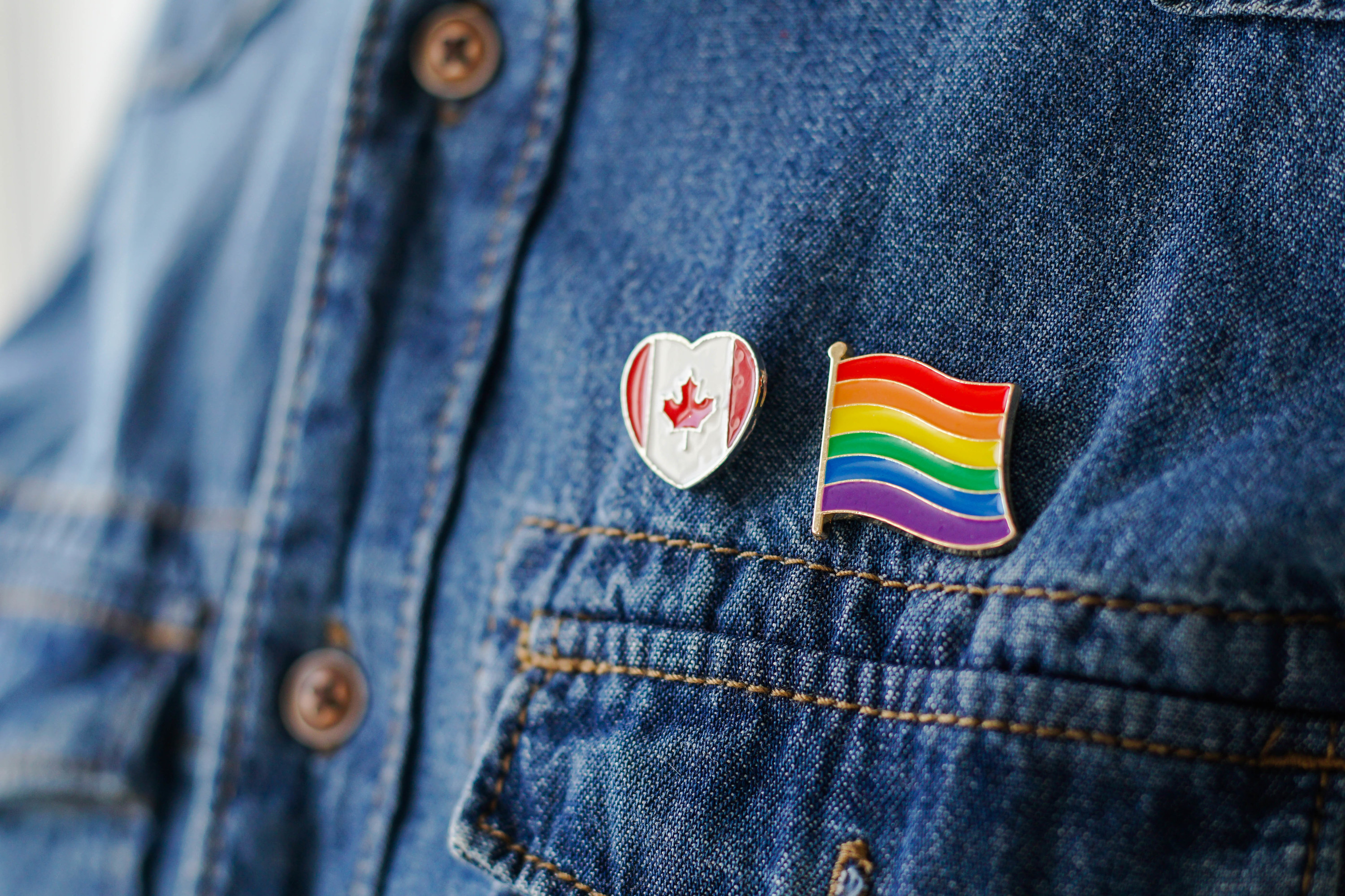 A Canadian flag and Pride flag pin on a jean jacket