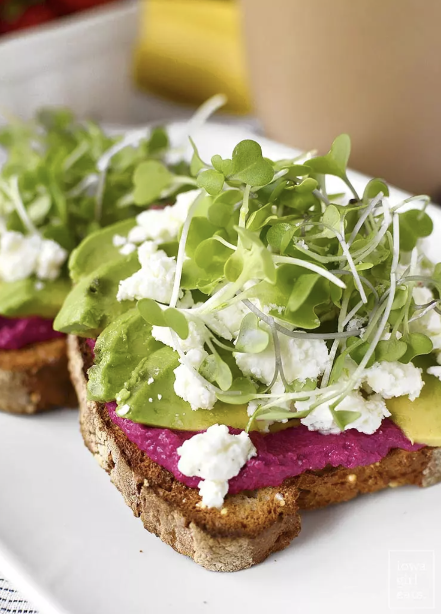 A slice of toast with beet hummus and avocado slices.