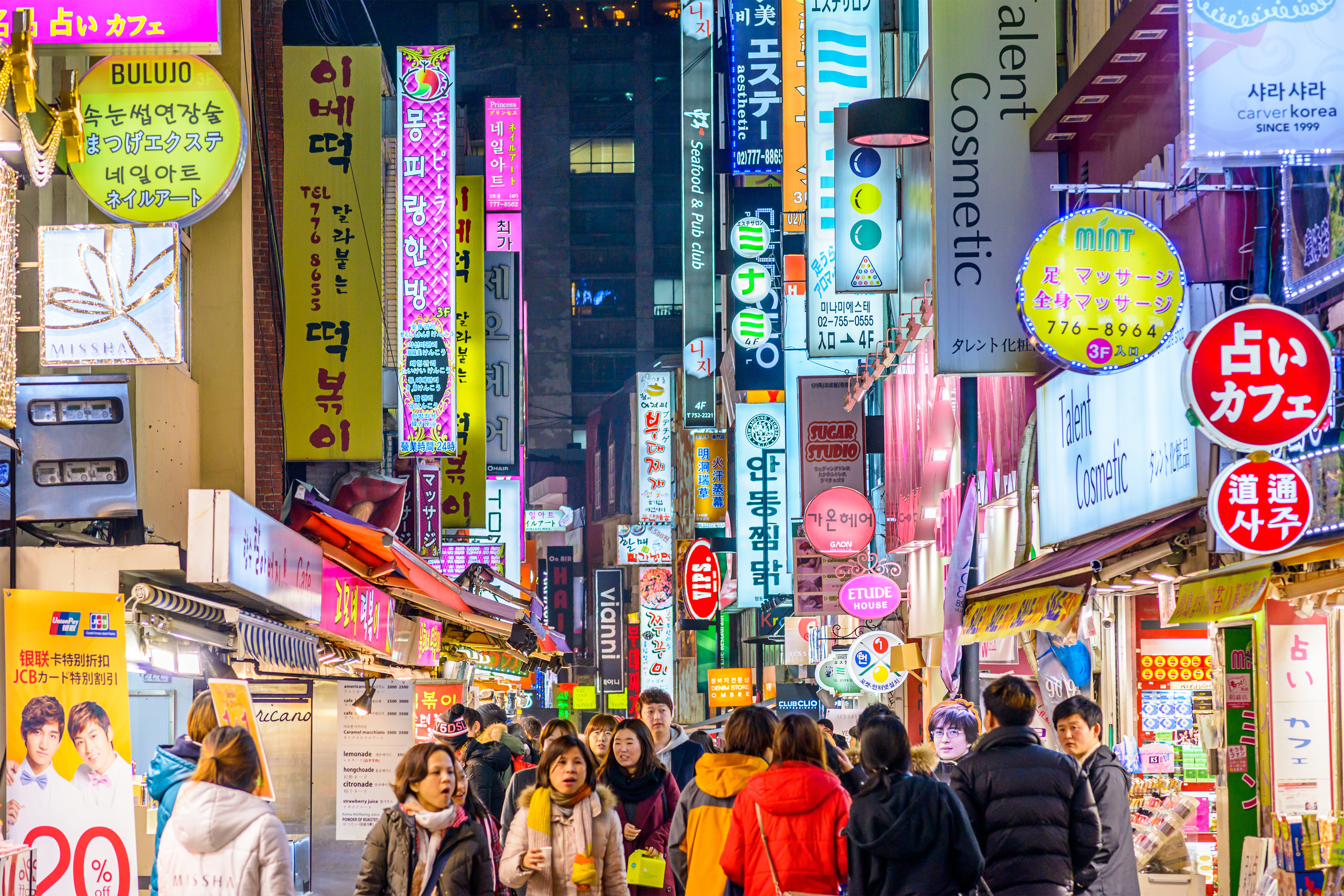 People walking around a busy South Korea street at night with vendors/stores on the side