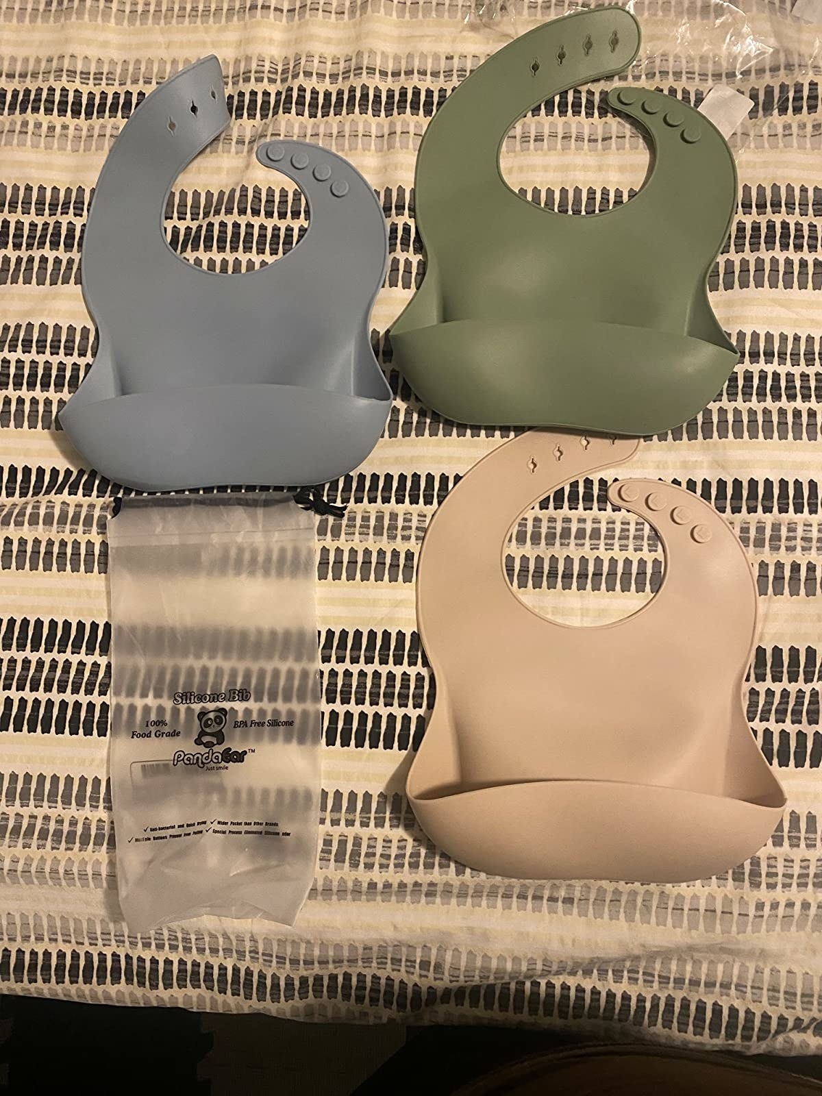 Reviewer&#x27;s photo of of three different colored bibs and the clear plastic bag they came in