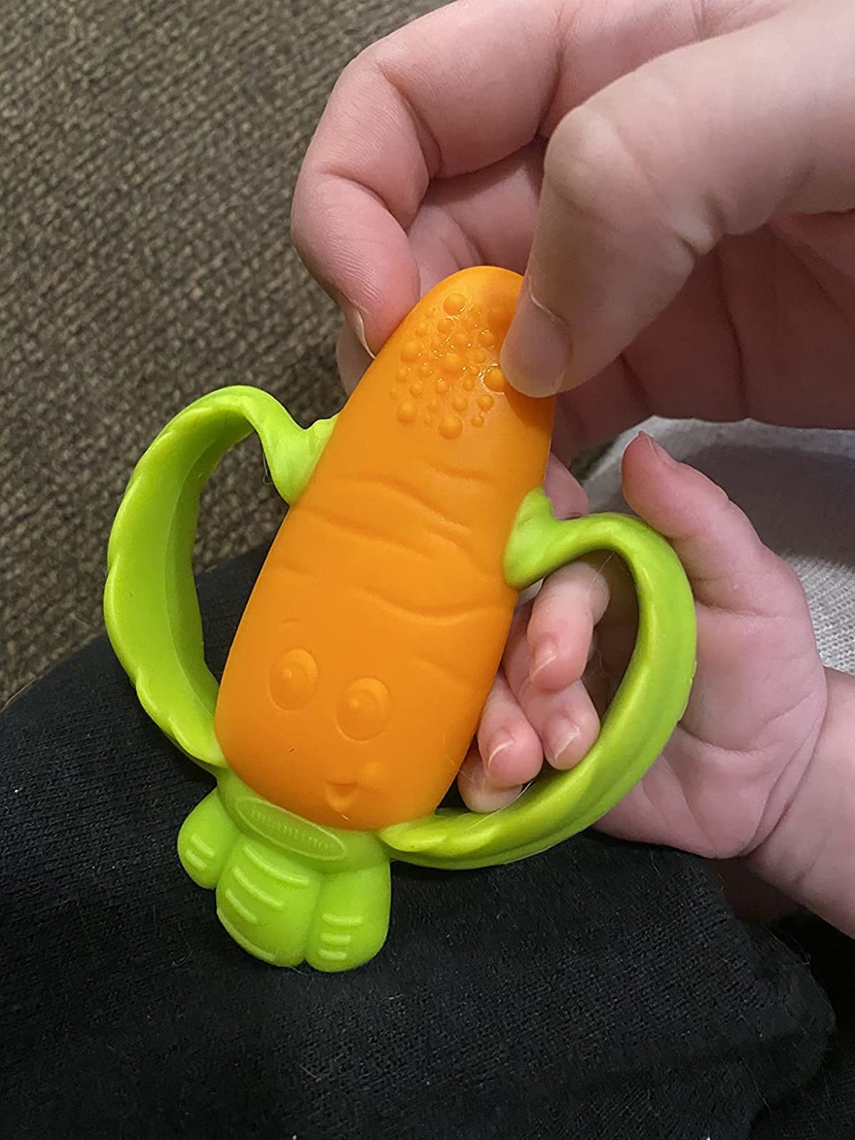 Reviewer&#x27;s photo of adult and baby hand holding green and orange carrot teether