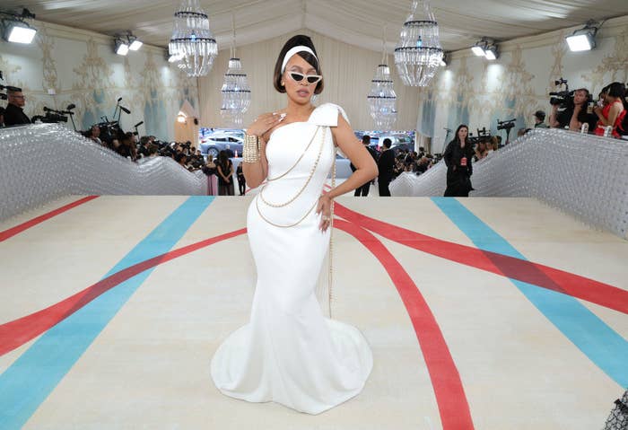 La La Anthony at the Met Gala wearing a one-shouldered gown with chains across it. She's also wearing cat-eye sunglasses and a headband