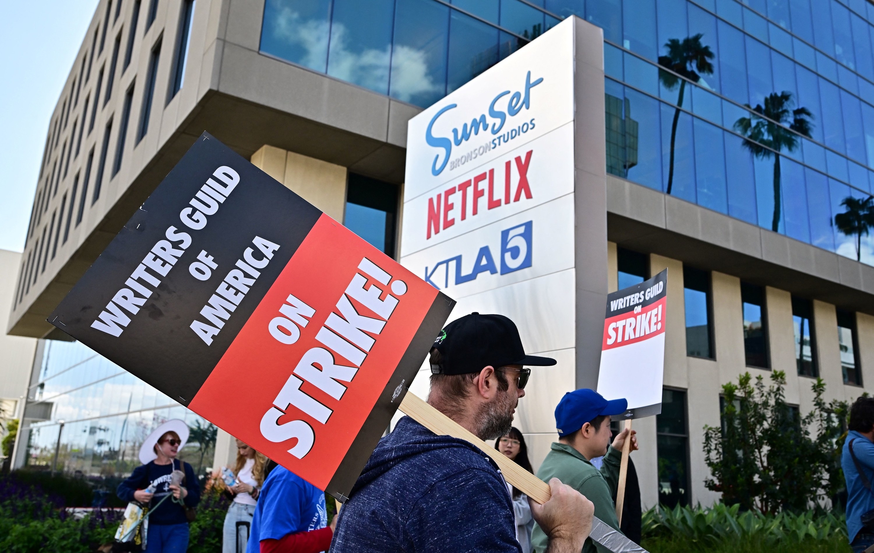A supporter of the Writers Guild of America holding a picket sign in front of a production building with a Netflix sign