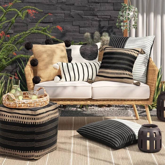 square white and black stripe outdoor lumbar throw pillow with tassels on top of wicker couch