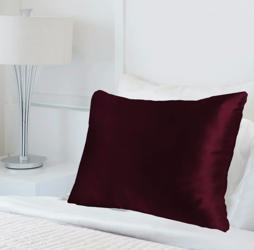 The burgundy silk pillowcase on a bed with a white comforter