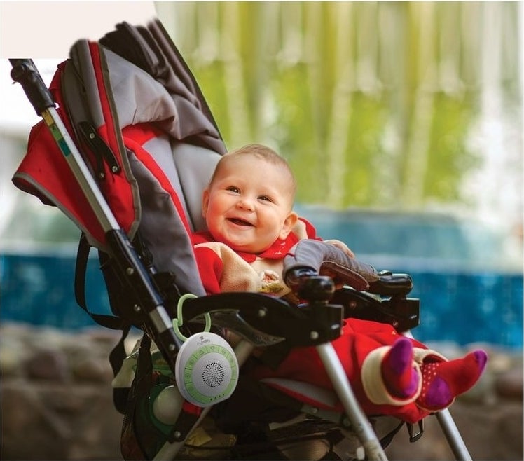 Sound machine hangs on a stroller as a baby smiles
