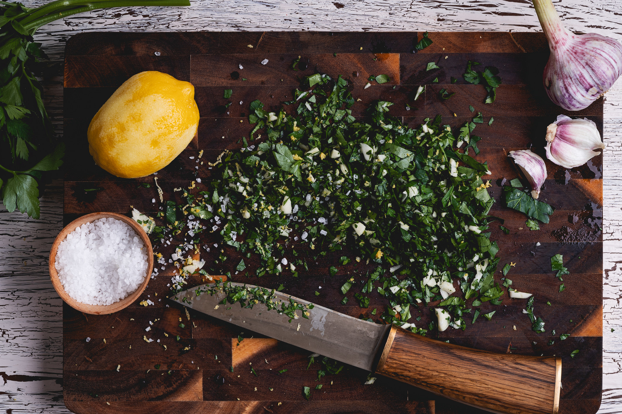 Chopped herbs, salt, lemon, and garlic on a cutting board.
