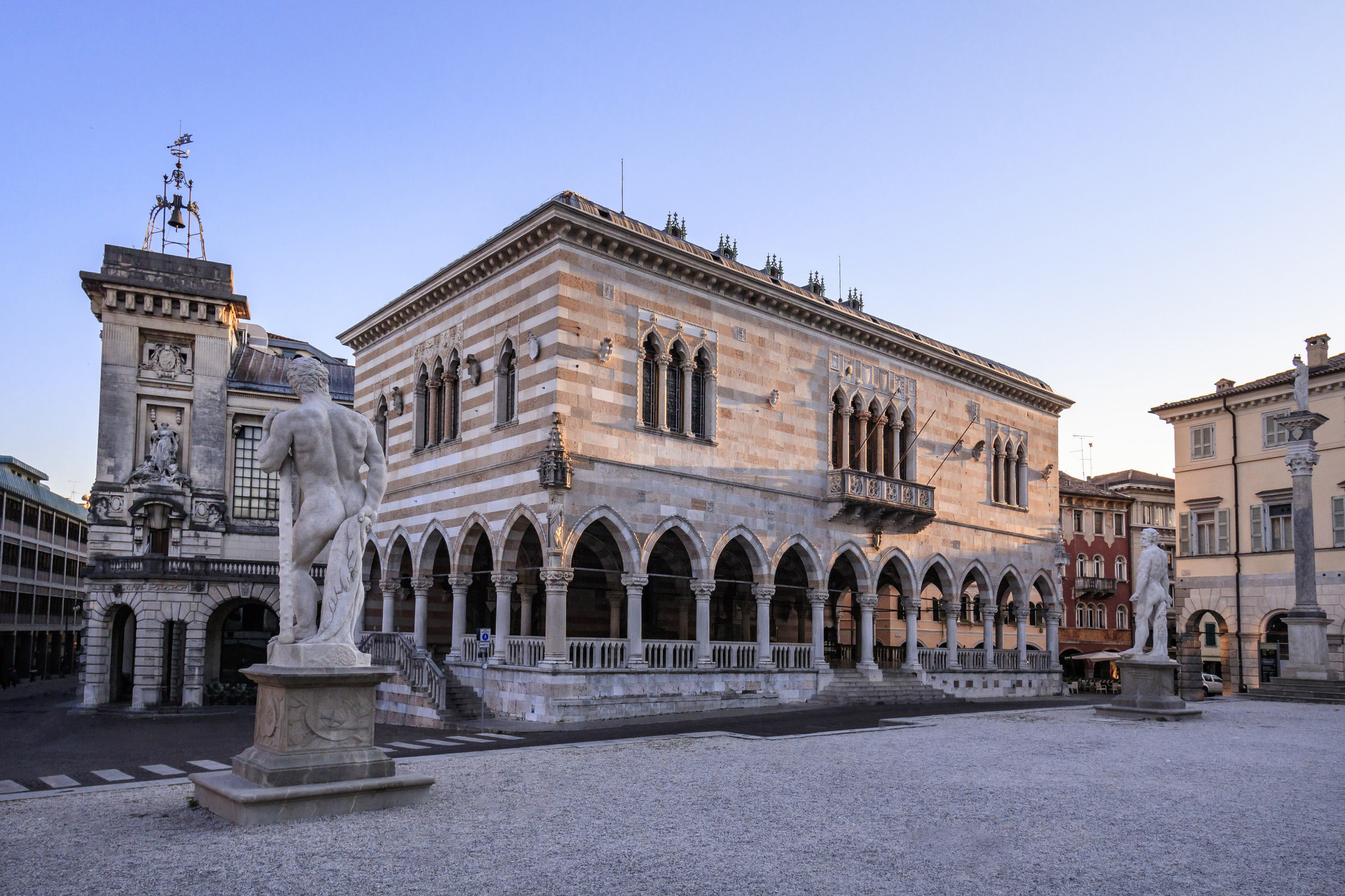 an old square in udine with large sculpture and stone buildings
