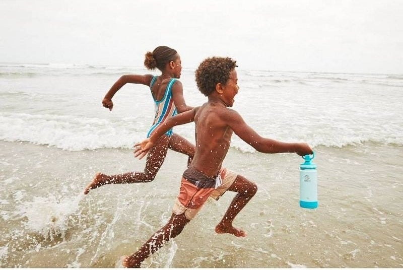 Kids run through water with a water bottle