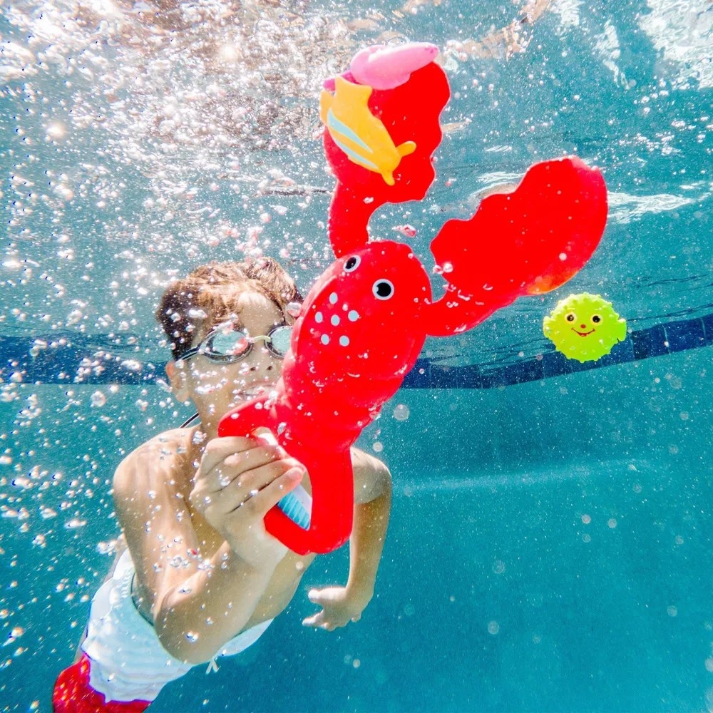 Child under water using a red lobster toy with colorful fish to catch with its claws