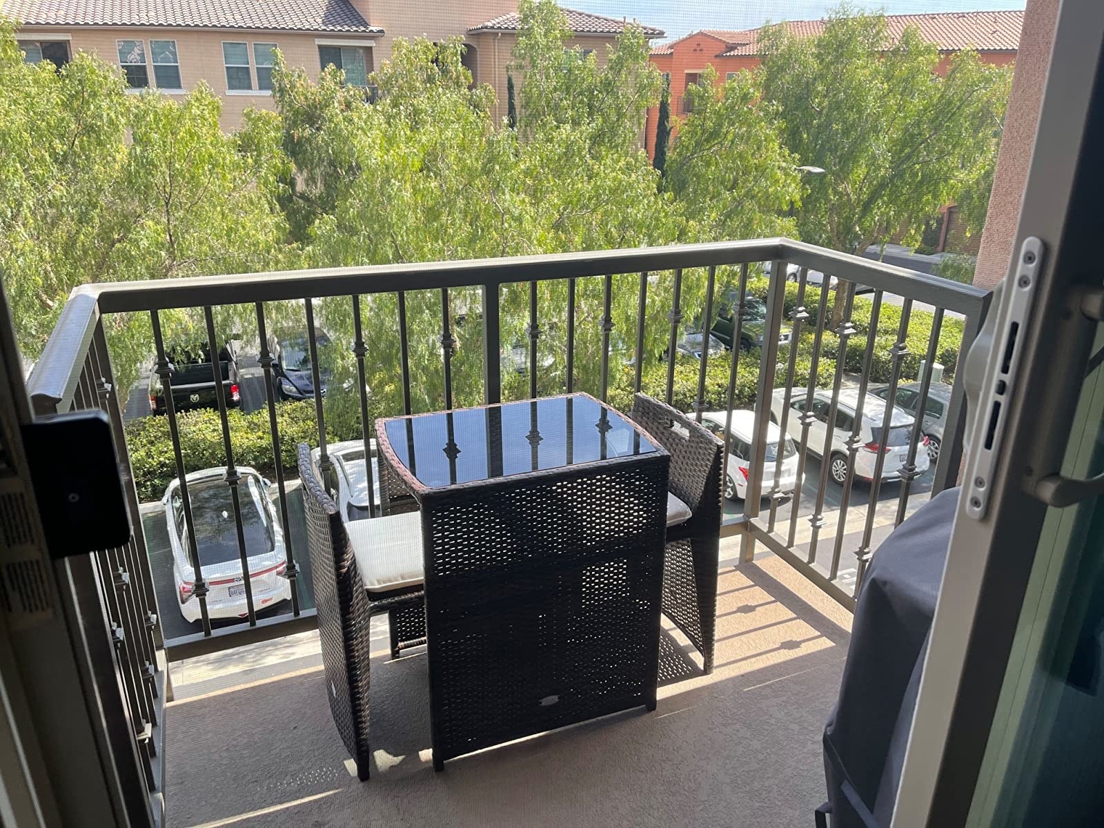 View of a small balcony with a wicker table and two chairs overlooking a parking area