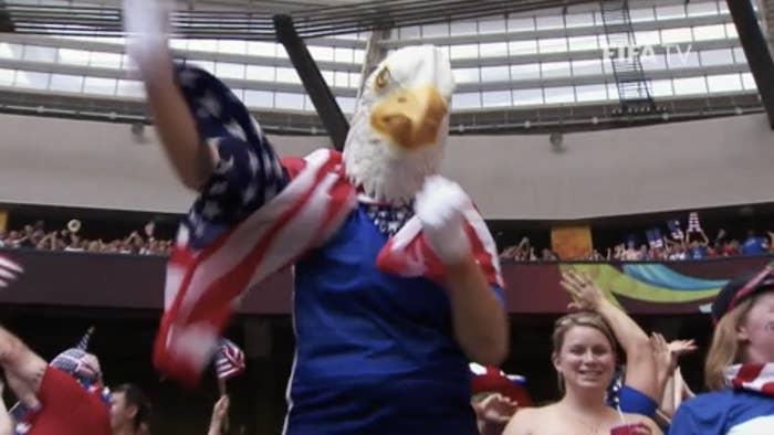 person in an eagle mask with an american flag over their shoulders