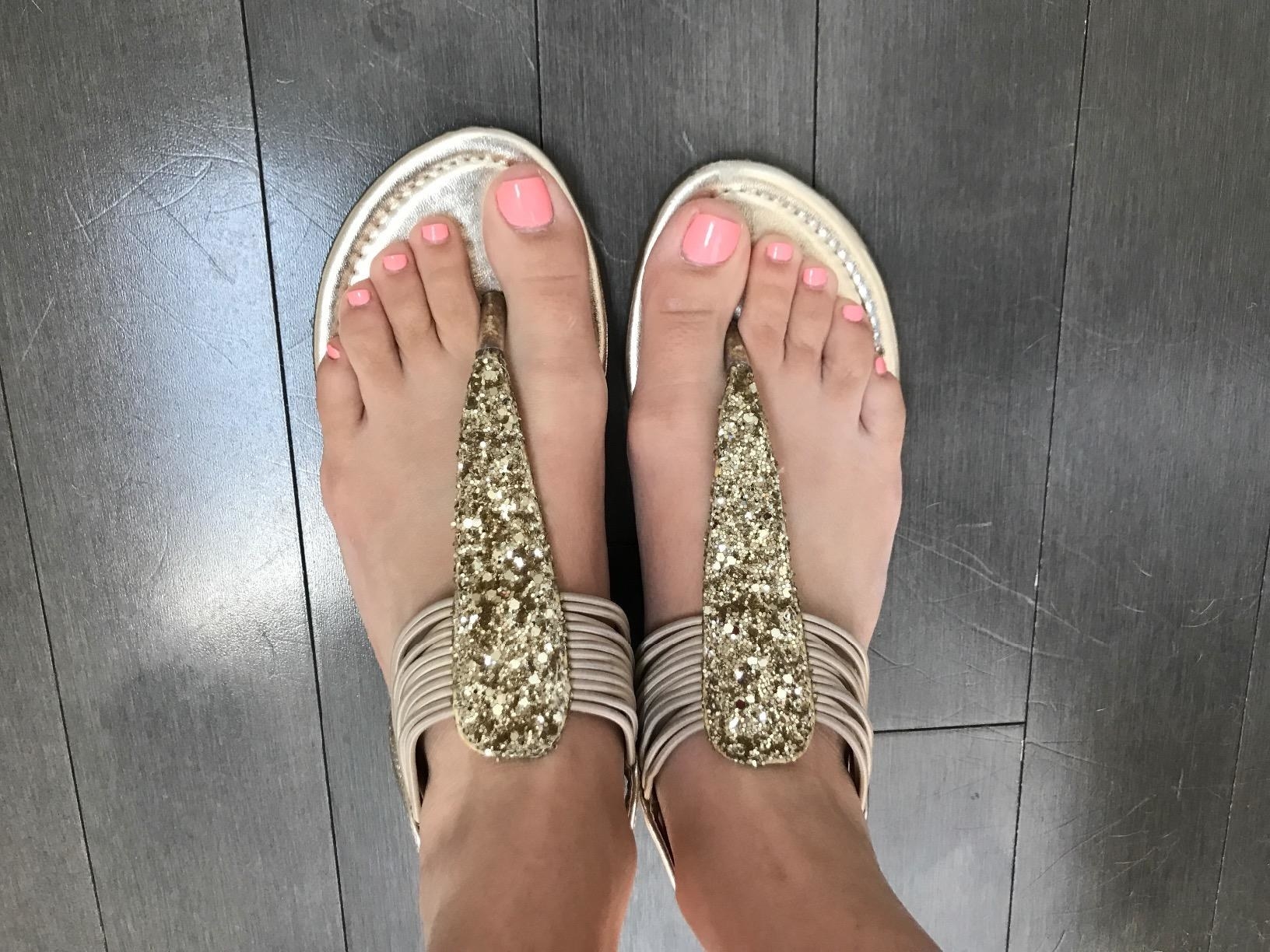 A reviewer wearing gold sandals with pink nail polish