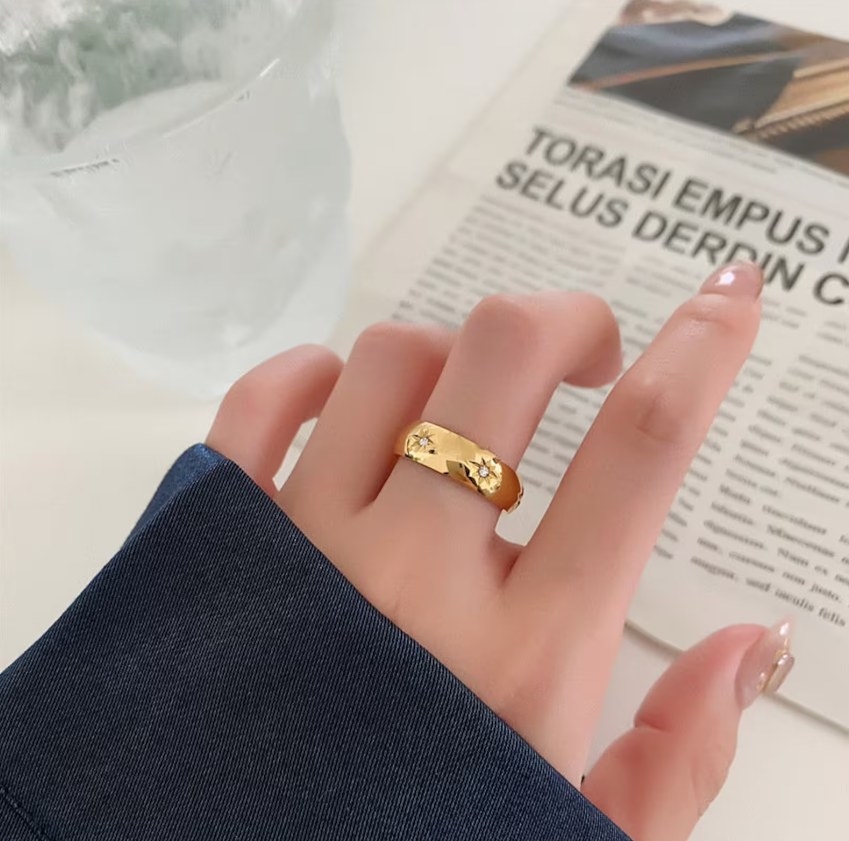 The gold colored ring worn on a model&#x27;s middle finger