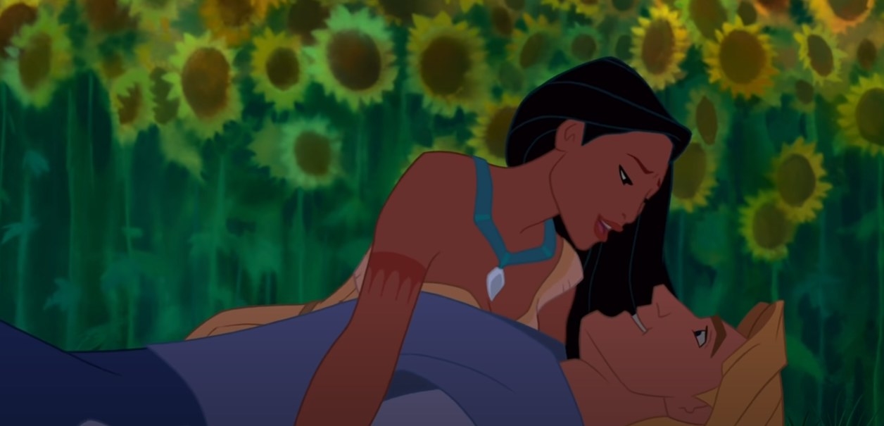 Disney&#x27;s Pocahontas and John Smith smiling at one another as she leans over him laying on the ground