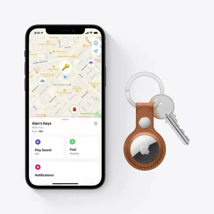 iPhone with tracking app open next to a set of keys with an AirTag attached