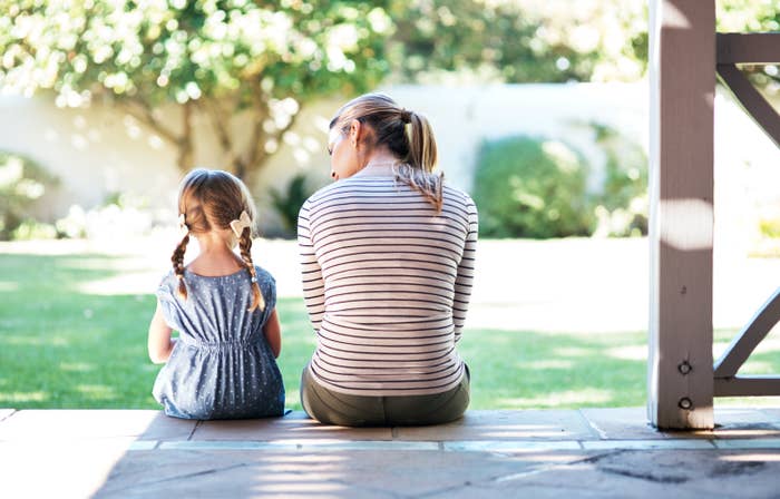 A woman talks to her young daughter on the porch of their home