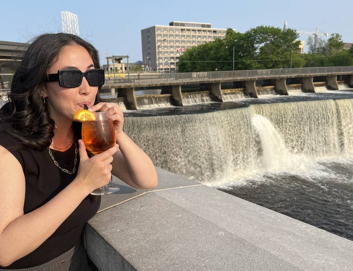 The writer sipping a drink while leaning on a railing that overlooks a waterfall