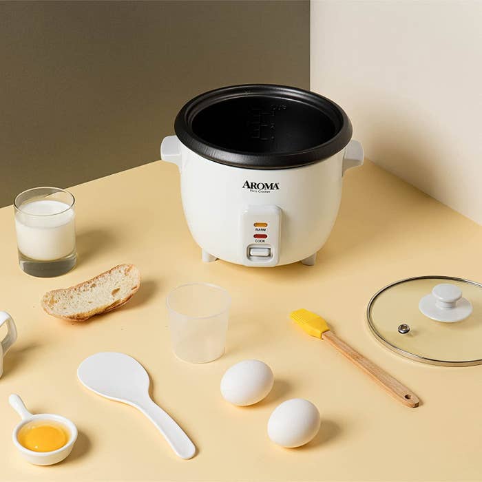 The rice cooker with supplies and utensils around it