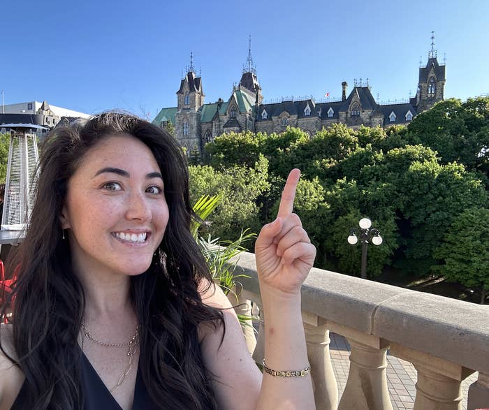 The writer posing for a photo on a balcony with Parliament buildings behind her