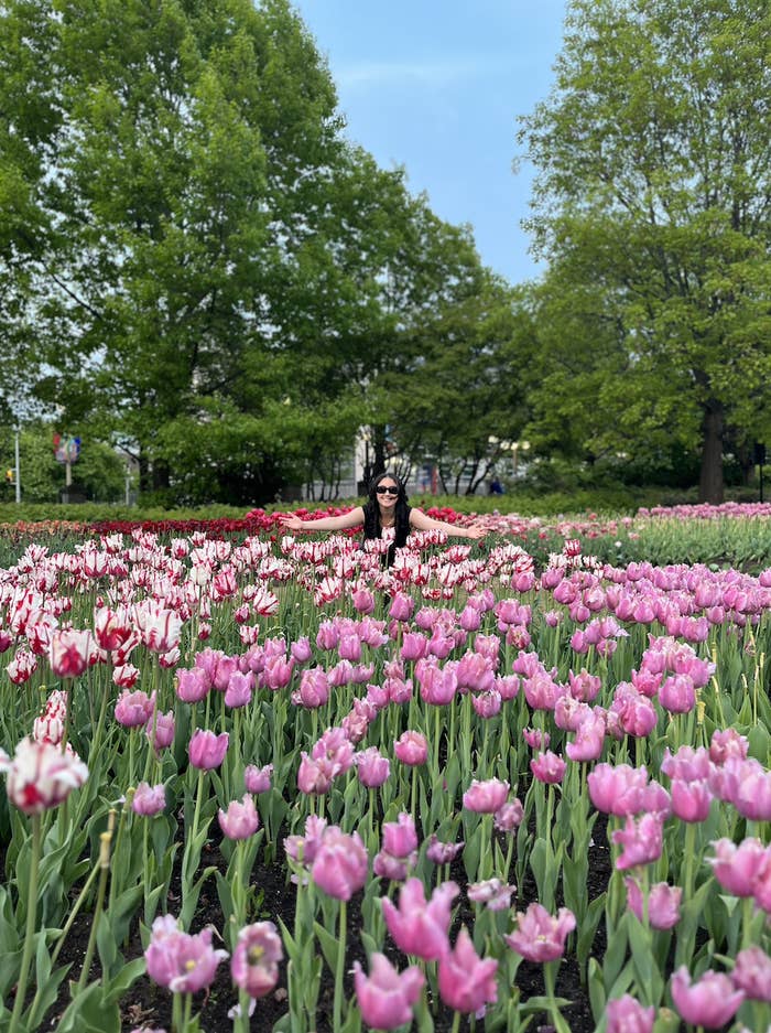 The writer with her arms spread in a garden, surrounded by flowers