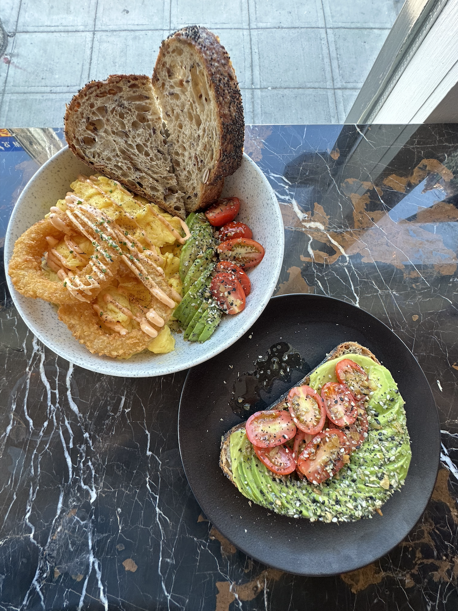 A plate of avocado toast has the avocados cut and fanned in a satisfying design, topped with tomatoes, salt, and pepper