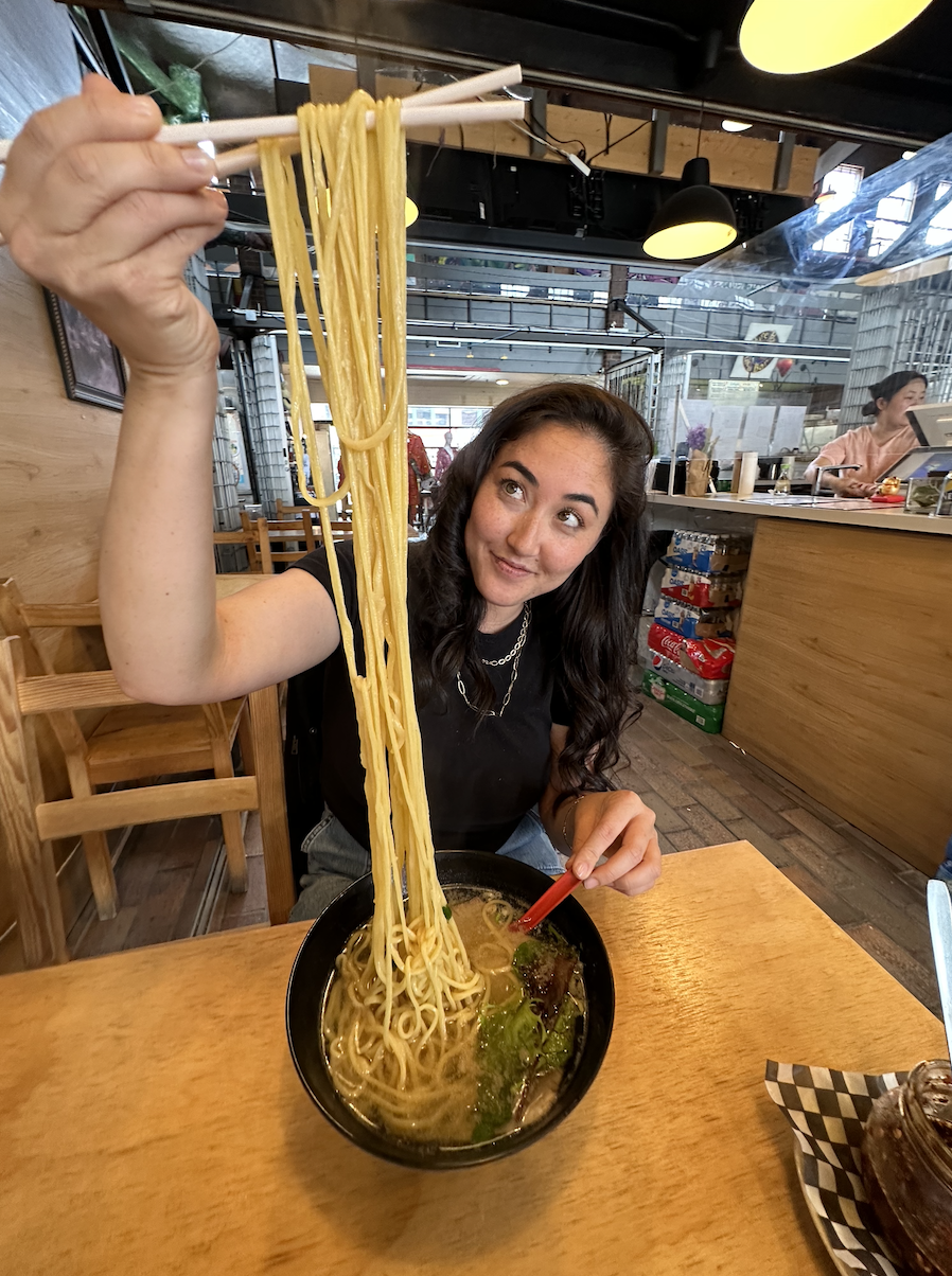 The writer using chopsticks to pull noodles so high that they&#x27;re above her head