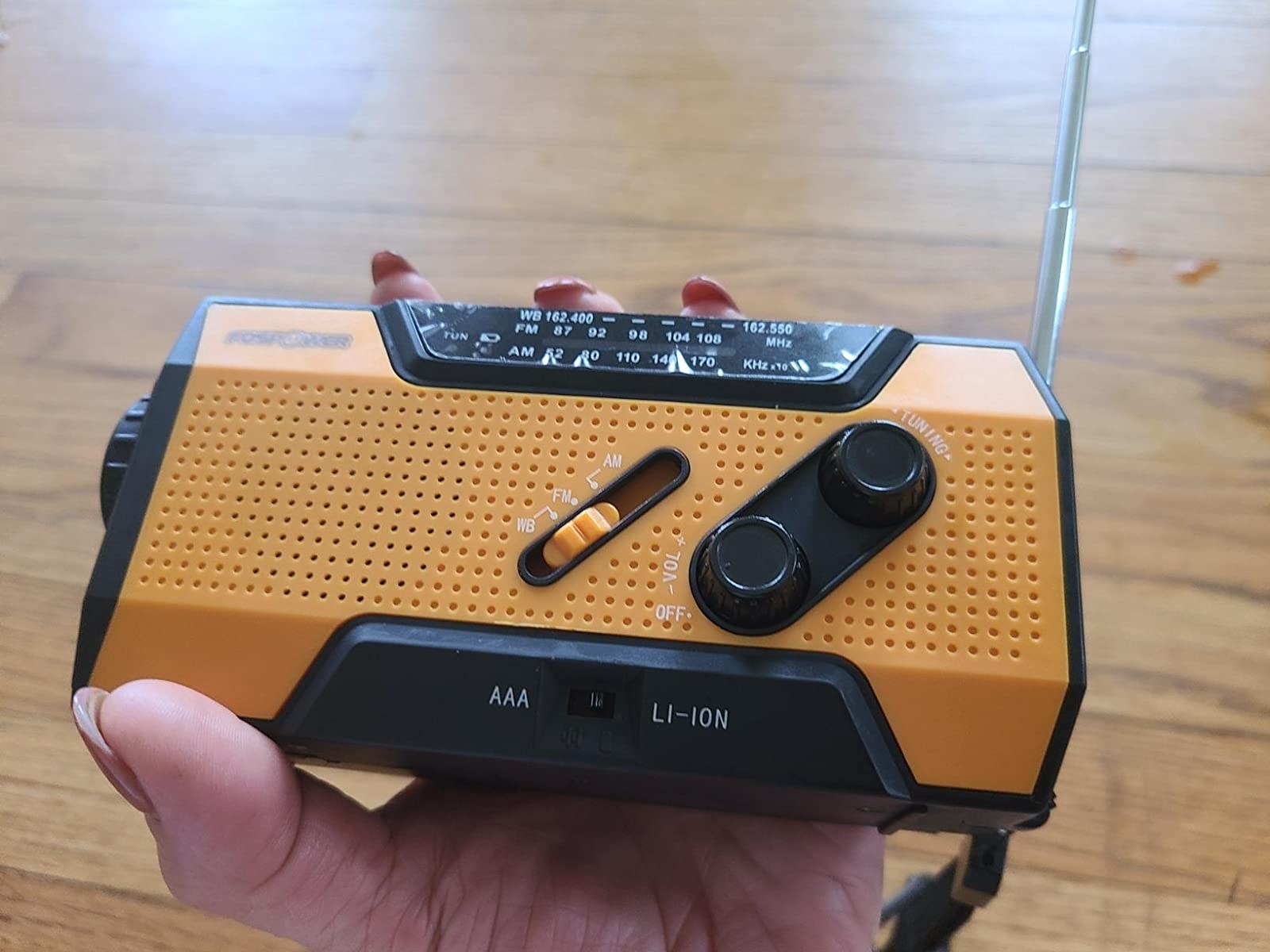 Reviewer&#x27;s photo of hand holding yellow and black emergency radio for scale