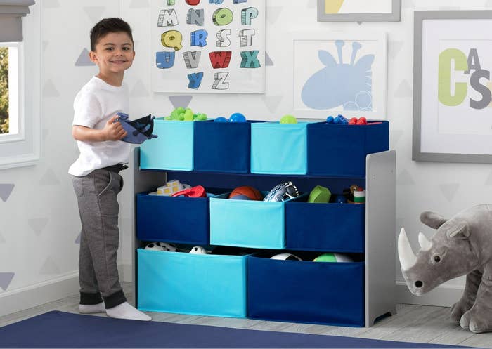 Child holding a toy boat next to a blue toy storage organizer.