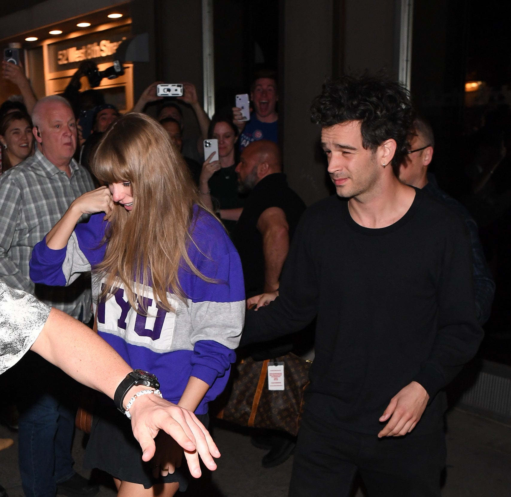 Taylor Swift and Matty Healy walking out of a building as people take photos of them