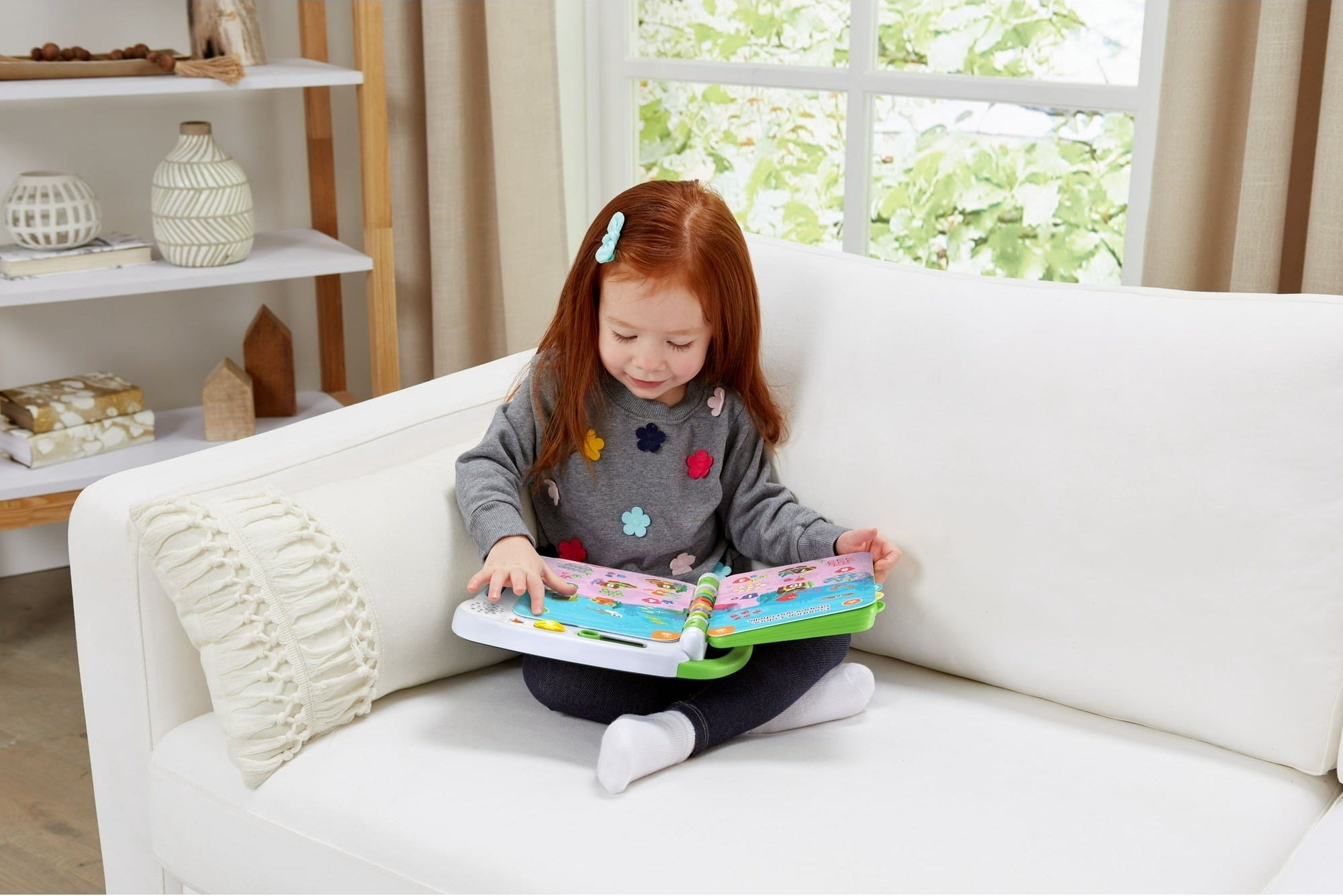 A little girl sitting on the couch playing with her activity book.