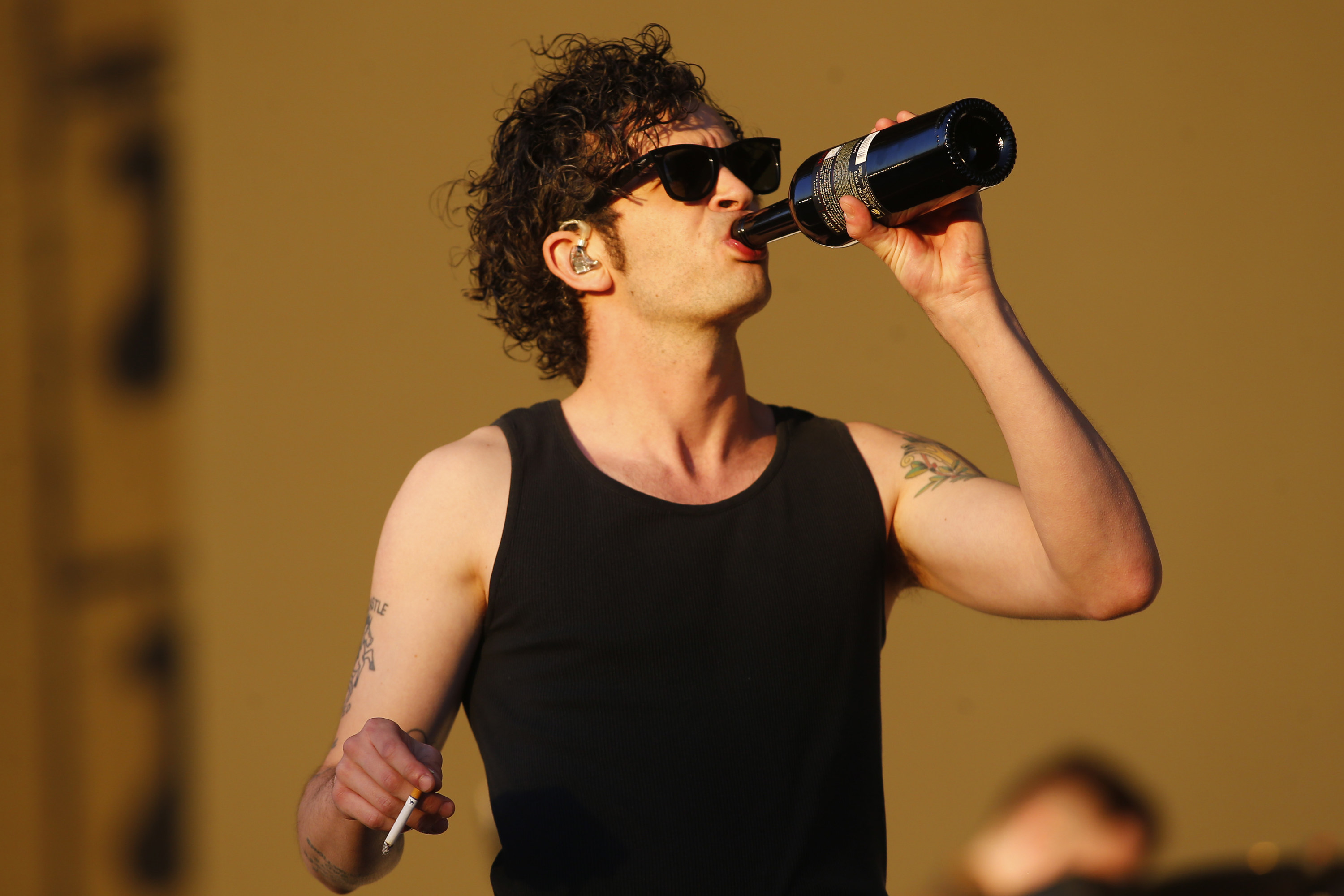 Matty Healy holding a cigarette and drinking straight from a bottle of wine