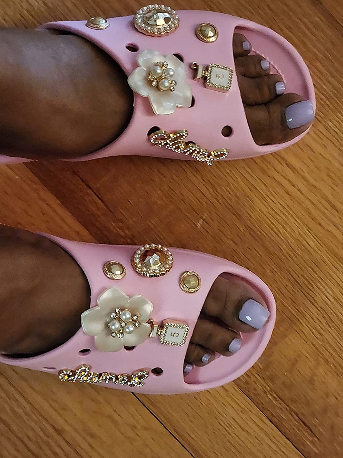 A reviewer wearing pink crocs with gold and white giblets
