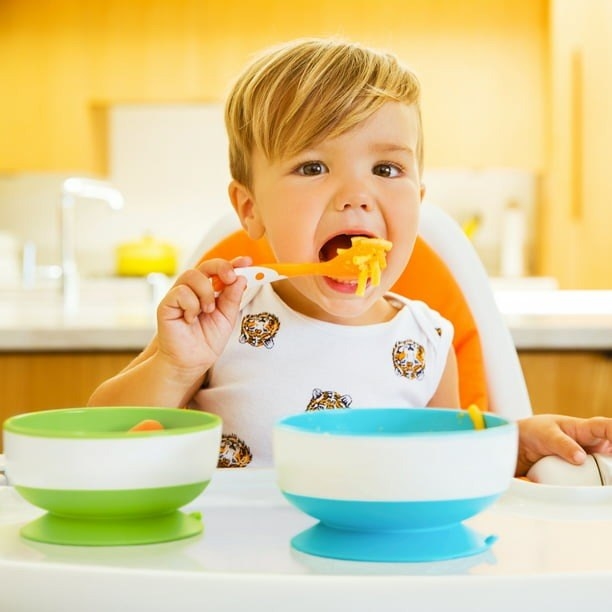 A child eating mac and cheese out of a blue suction bowl.