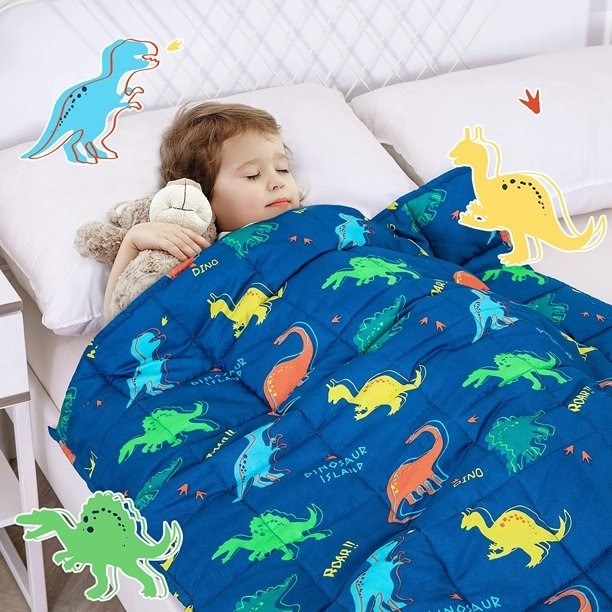 A child sleeping in bed with a dinosaur weighted blanket.