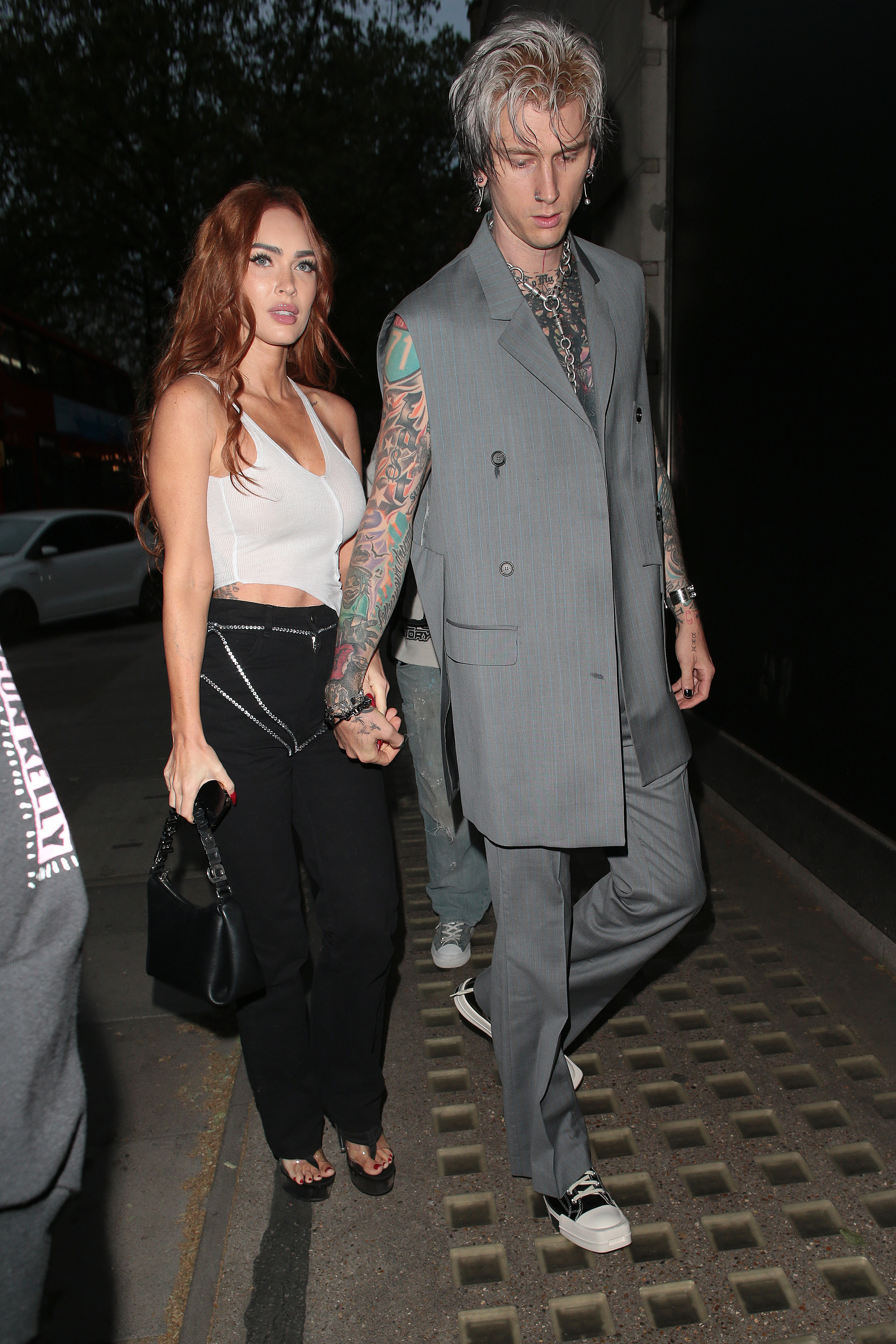 Megan and MGK holding hands as they walk towards a building at night