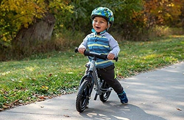 A toddler in a helmet riding the balance bike on the sidewalk.