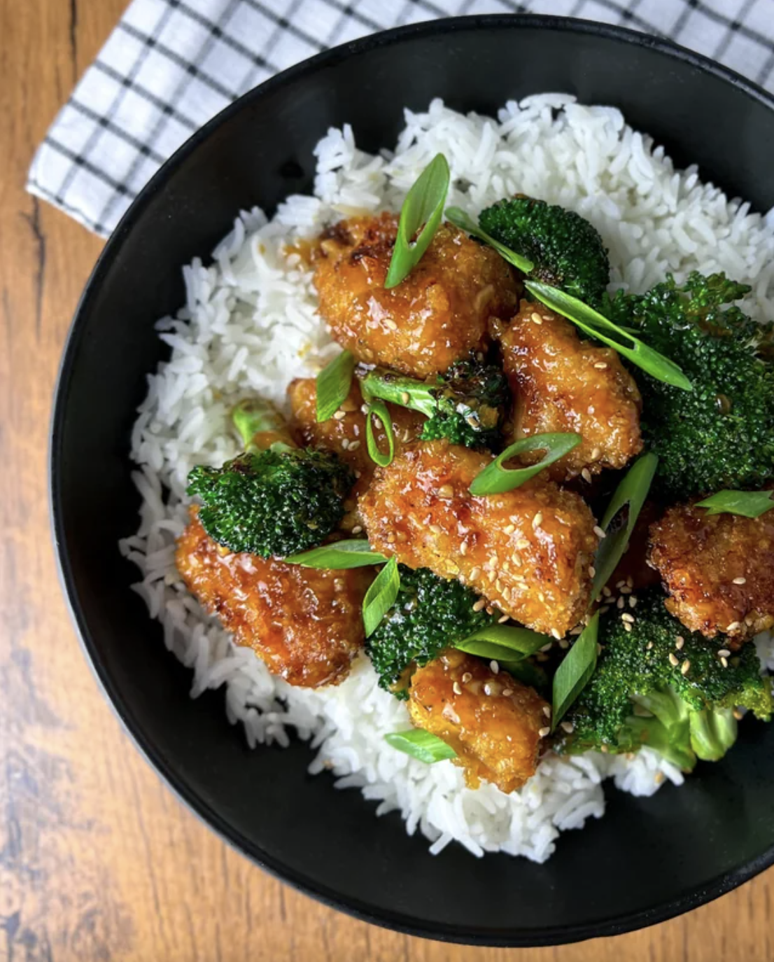 bowl of white rice topped with orange chicken broccoli and scallions
