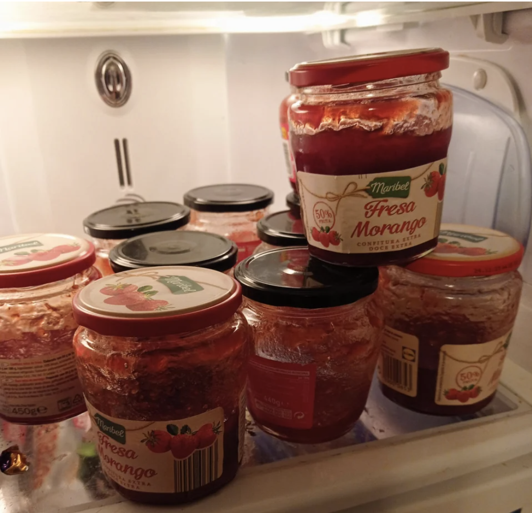 Around 10 half-finished jars of jam on a refrigerator shelf