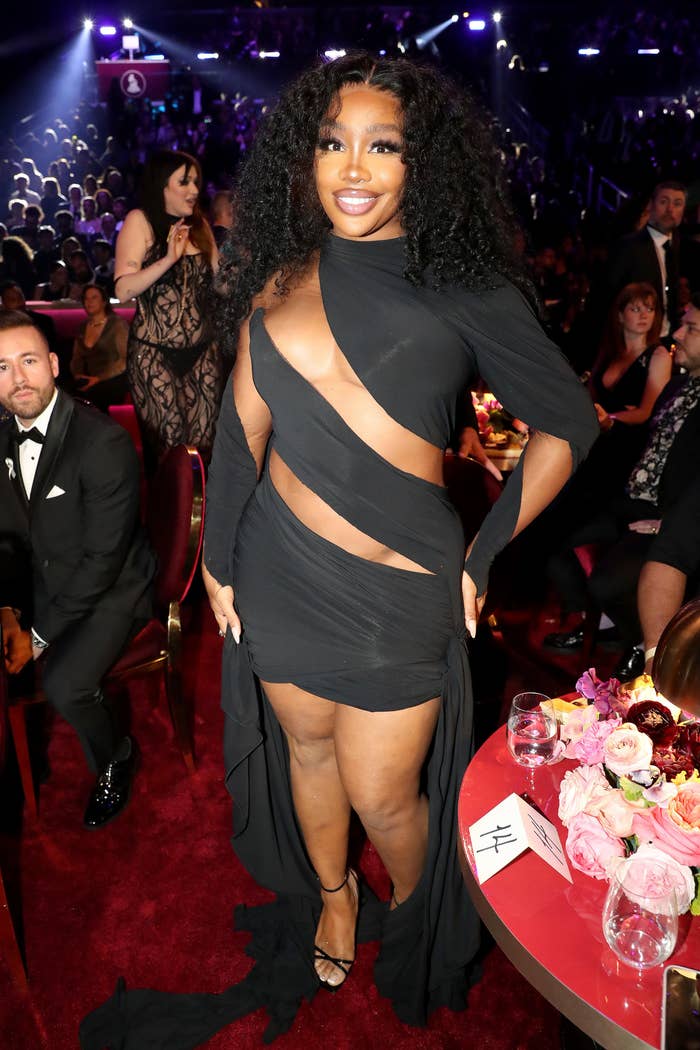 SZA smiles for the camera as she stands next to a round dinner table at an event