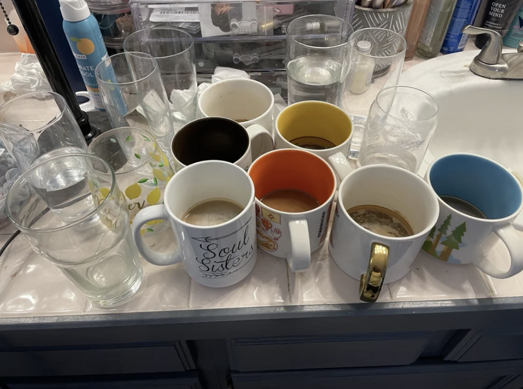 More than a dozen glasses and mugs with liquid still in them resting on a countertop