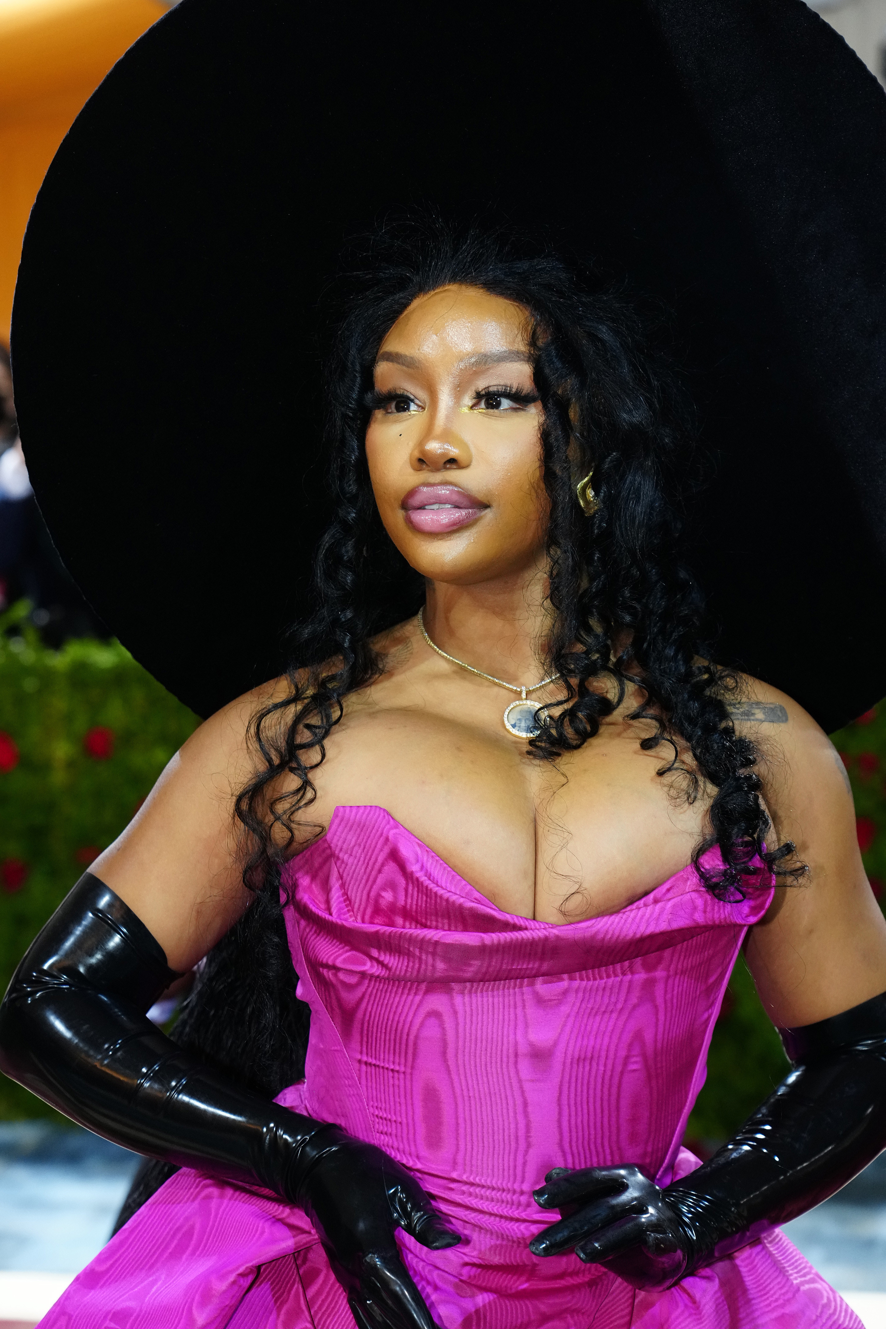 Closeup of SZA in a strapless structured gown and a wide-brimmed hat and patent leather opera length gloves